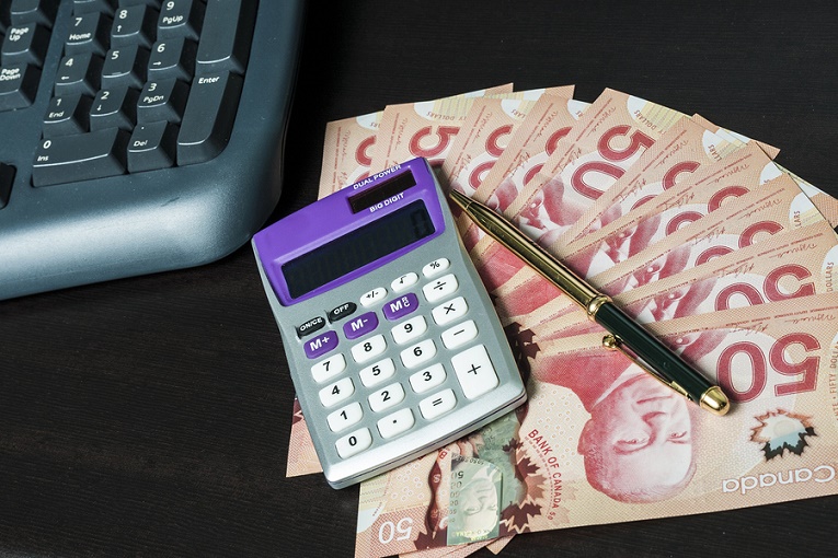 pen, calculator on top of Canadian pink 50 dollar bills next to keyboard