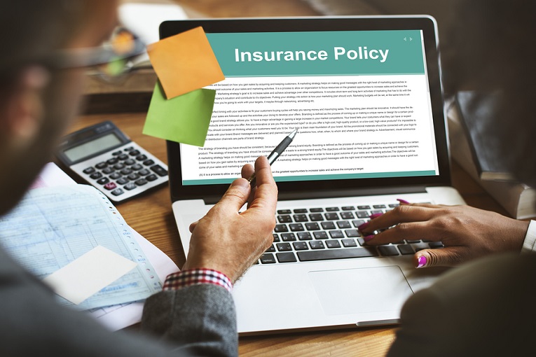 "insurancep olicy on laptop on desk with sticky notes and calculator"