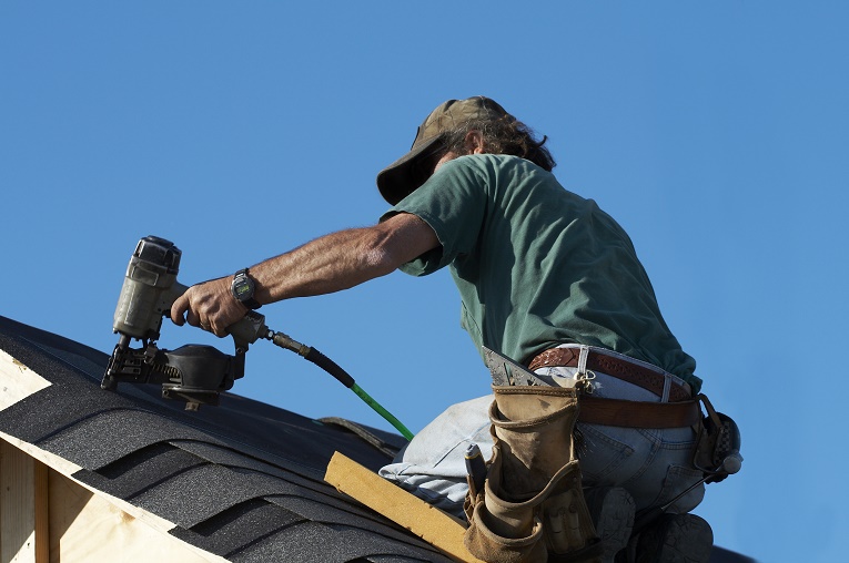 man nailing shingles on roof