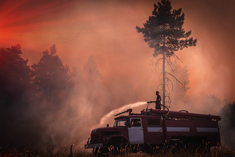 "fireman on top of truck spraying water"