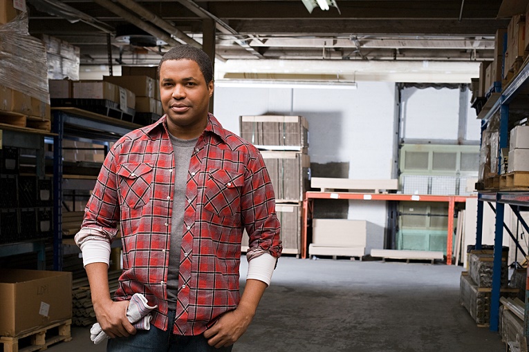 "man in flannel shirt standing in warehouse staring"