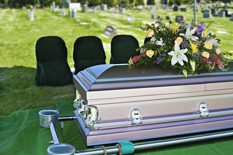 "coffin with flowers on top in graveyard"