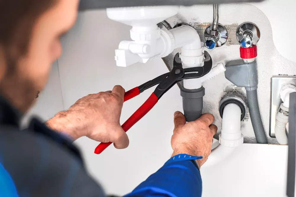 plumber working on pipes under a sink
